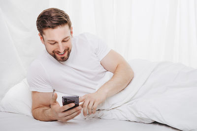 Young man using phone while lying on bed at home
