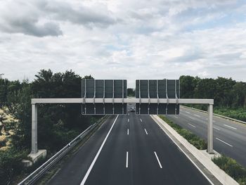 Signboard over highway against cloudy sky