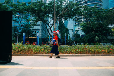 Woman walking on footpath by building in city