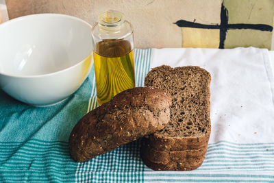 Close-up of brown bread with olive oil bottle on tablecloth at table