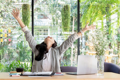 Happy businesswoman with arms raised sitting at desk in office