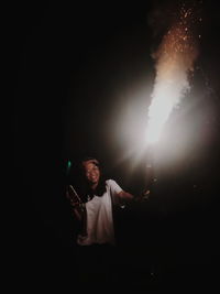 Portrait of smiling woman holding illuminated firework display at night
