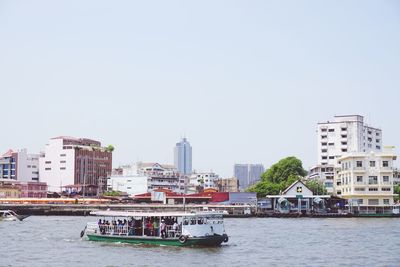 Boats in river by buildings against clear sky