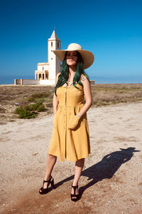 Full length portrait of smiling young woman standing against clear sky