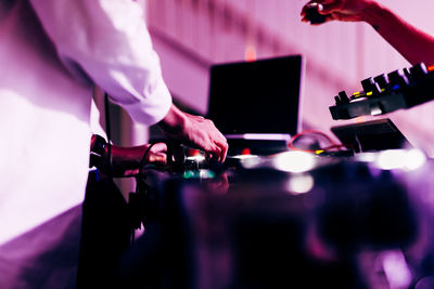 Dj is playing music in a nightclub. you can see his hands mixing music with his dj mixer 