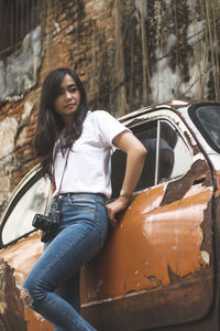 Low angle view of young woman smiling while standing by abandoned car