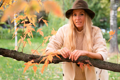 Portrait of young woman standing by tree trunk