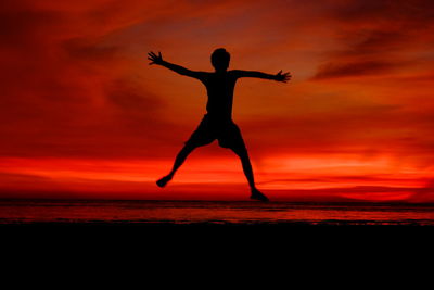 Full length of silhouette man jumping at beach against orange sky