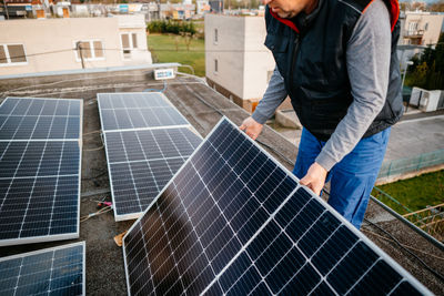 Rear view of man working with solar panel on roof