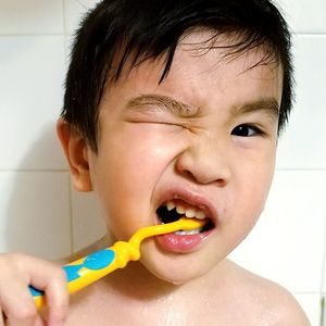 Close-up portrait of boy brushing teeth in bathroom
