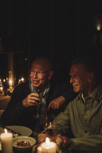 Happy senior male friends enjoying candlelight dinner together at party