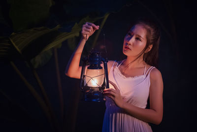 Woman holding illuminated lantern while standing outdoors at night