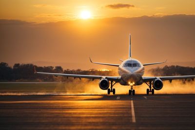 Airplane on airport runway against sky during sunset