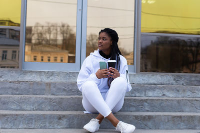 Young woman using phone while sitting on staircase