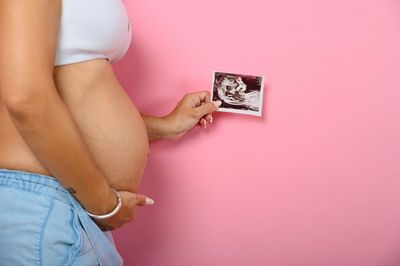 Midsection of woman holding pink umbrella against wall