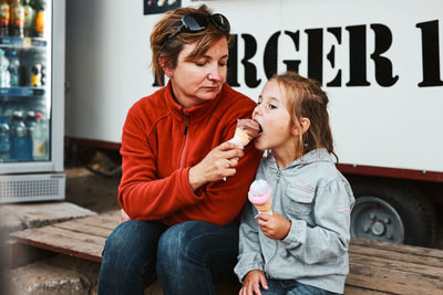 Mother and her daughter eating ice cream sitting on a step in front of food truck during vacation