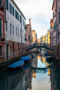 Boats moored in canal by buildings against sky in city