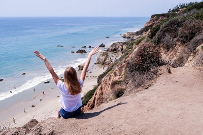 Rear view of woman sitting on cliff against sea