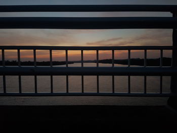 Silhouette railing by sea against sky during sunset