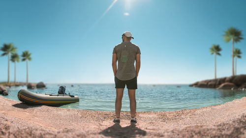 Rear view of man standing on beach against clear sky