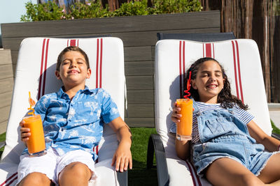 Two little kids sunbathing with a orange juice