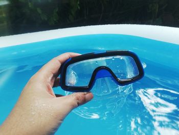 Close-up of hand holding sunglasses in swimming pool
