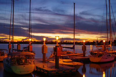 Sailboats moored at illuminated harbor against sky during sunset