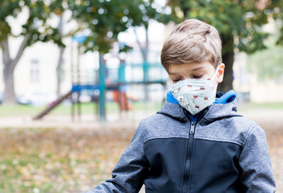 Boy with face mask feeling sad because he has no one to play with on the playground due to covid-19.