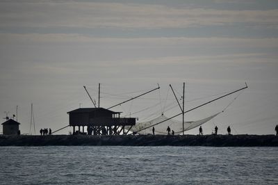 Silhouette cranes by sea against sky during sunset