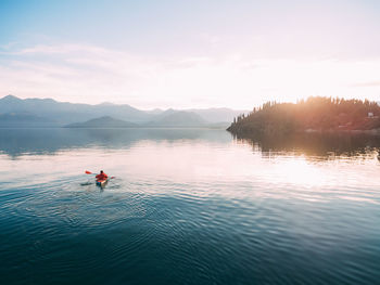 People in lake against sky during sunset