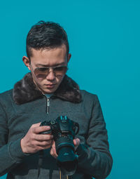 Young man photographing with camera against gray background