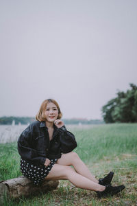 Young woman sitting on field against sky