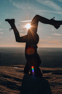 Full length of woman doing handstand on rock against sky during sunset