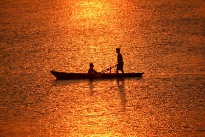 Silhouette people on boat in sea against orange sky