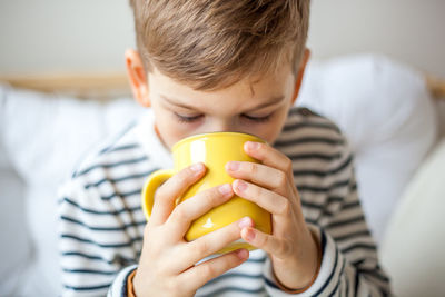 High angle view of boy drinking coffee while sitting on bed at home