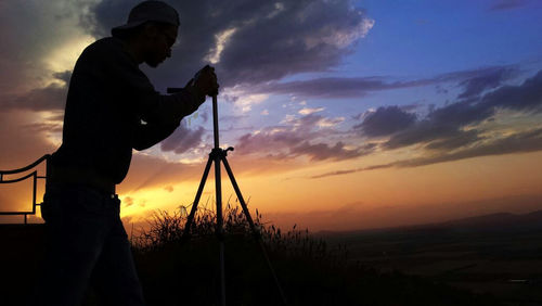 Silhouette man photographing against sky during sunset
