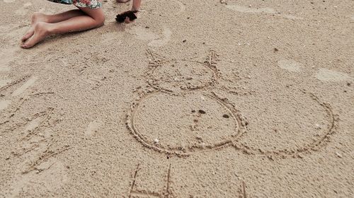 Low section of girl kneeling beside drawing in sand