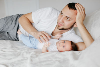 Man lying down with baby on bed at home