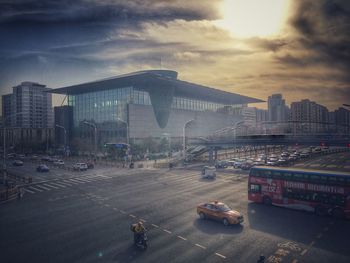 Vehicles on road by buildings against sky during sunset