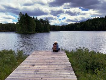 Woman sitting on wood by lake against sky