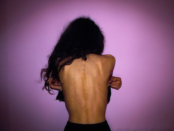 Rear view of shirtless woman standing against purple wall