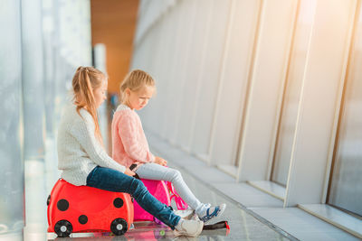 Side view of girls sitting on bag at airport