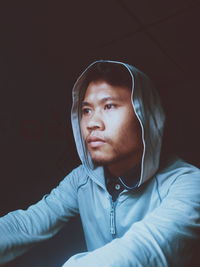 Young man in hood looking away on black background