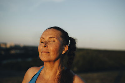 Sportswoman with eyes closed against sky during sunset