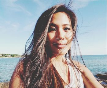 Portrait of beautiful young woman at beach against sky