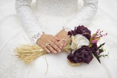 Midsection of woman holding bouquet against white wall
