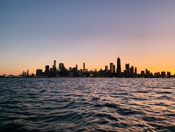 Sea and buildings against clear sky during sunset