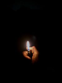 Close-up of hand holding lit candle in darkroom