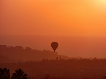 Silhouette hot air balloon flying against orange sky