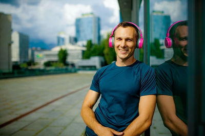 Happy man with pink earphones relaxing in city street.